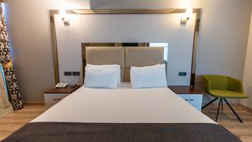 Una habitación de hotel moderna con una cama grande, mesitas de noche, una silla verde y un espejo sobre la cama.