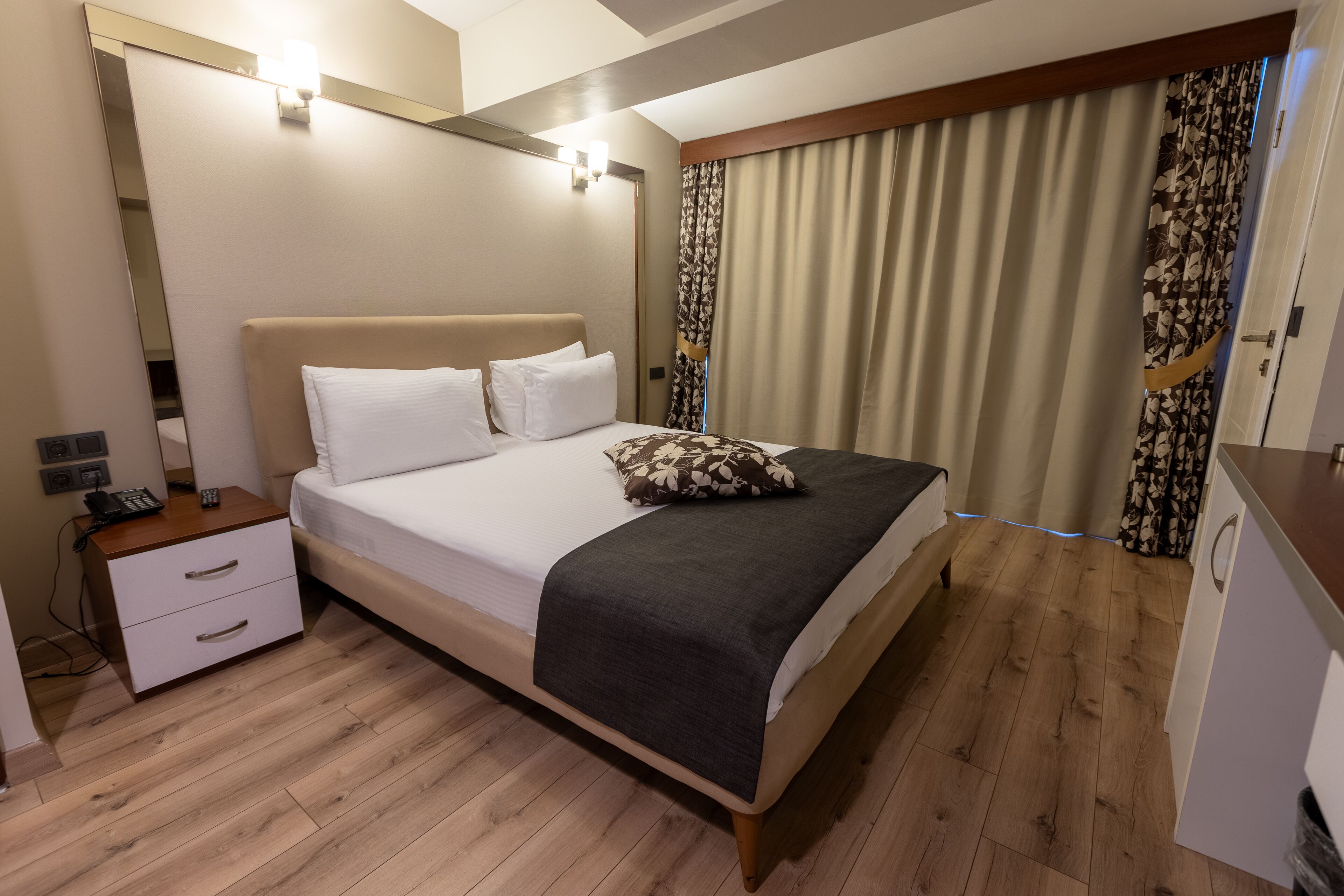 A hotel room with a bed, bedside table, and a mirror.