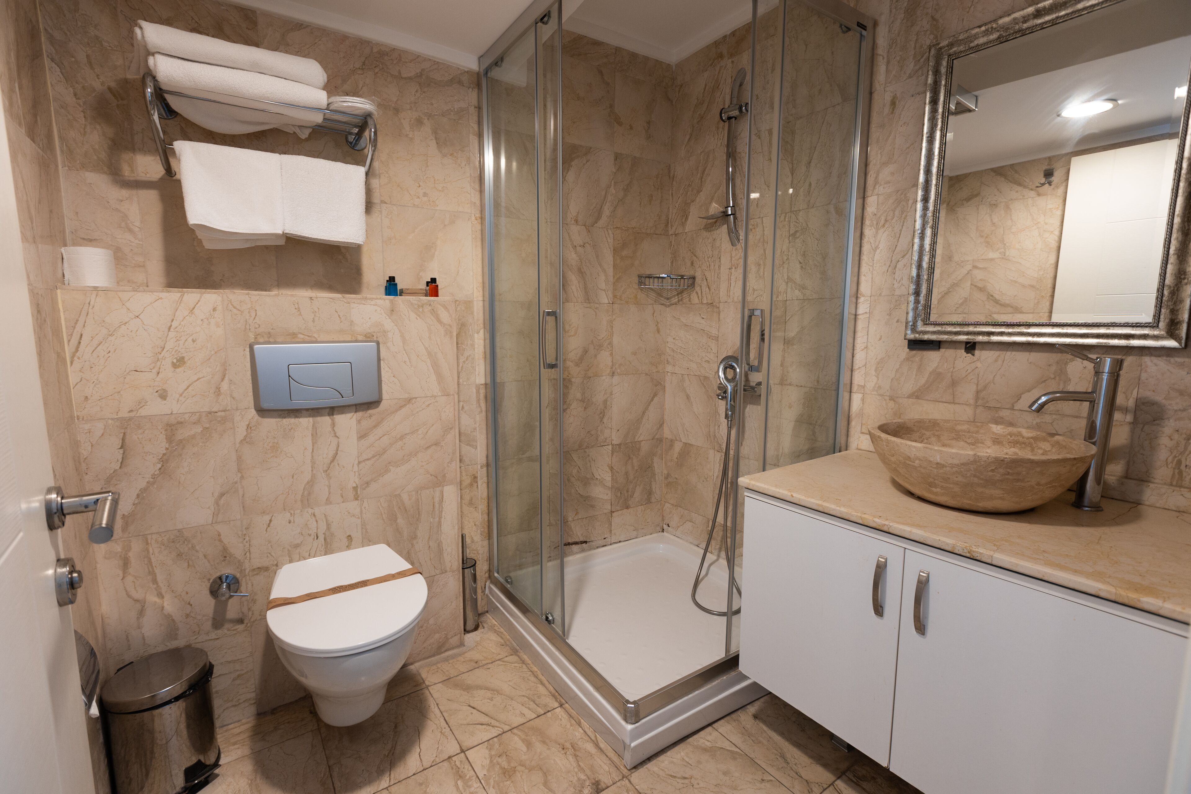 A modern bathroom with a glass-enclosed shower, a white toilet, and a wooden basin sink.