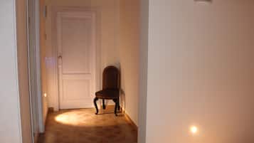 Un corridoio stretto con una sedia di legno, una porta bianca e un piccolo lampadario a parete.