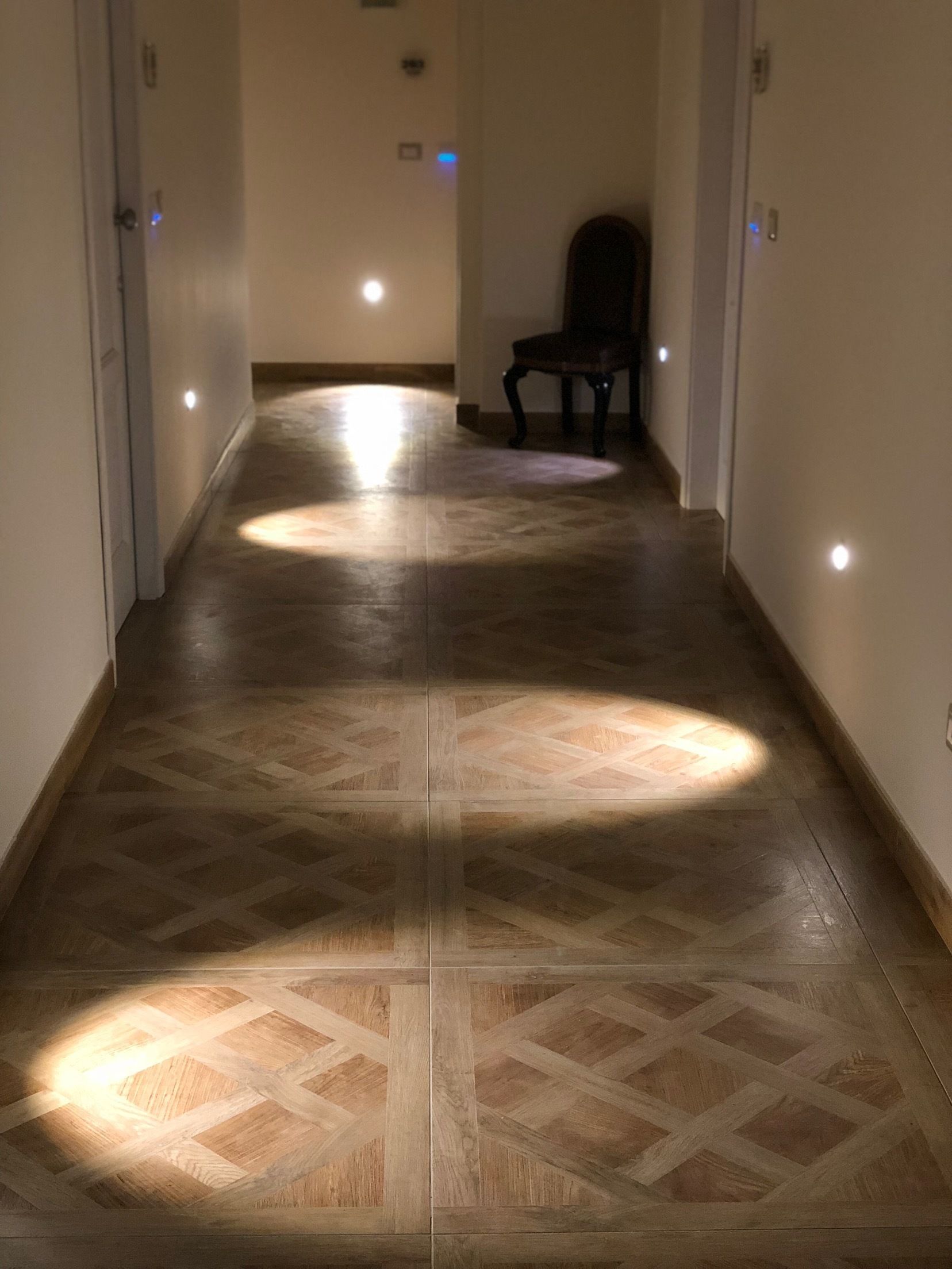 A hallway with patterned flooring and recessed lighting.