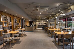 A modern cafe interior with wooden tables and chairs, a reception desk, and a variety of decorative items on shelves. - Upsuites Hotel (Istanbul)