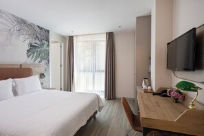 A hotel room with a large bed, a desk with a lamp, a television, and a painting on the wall. - Upsuites Hotel (Istanbul)