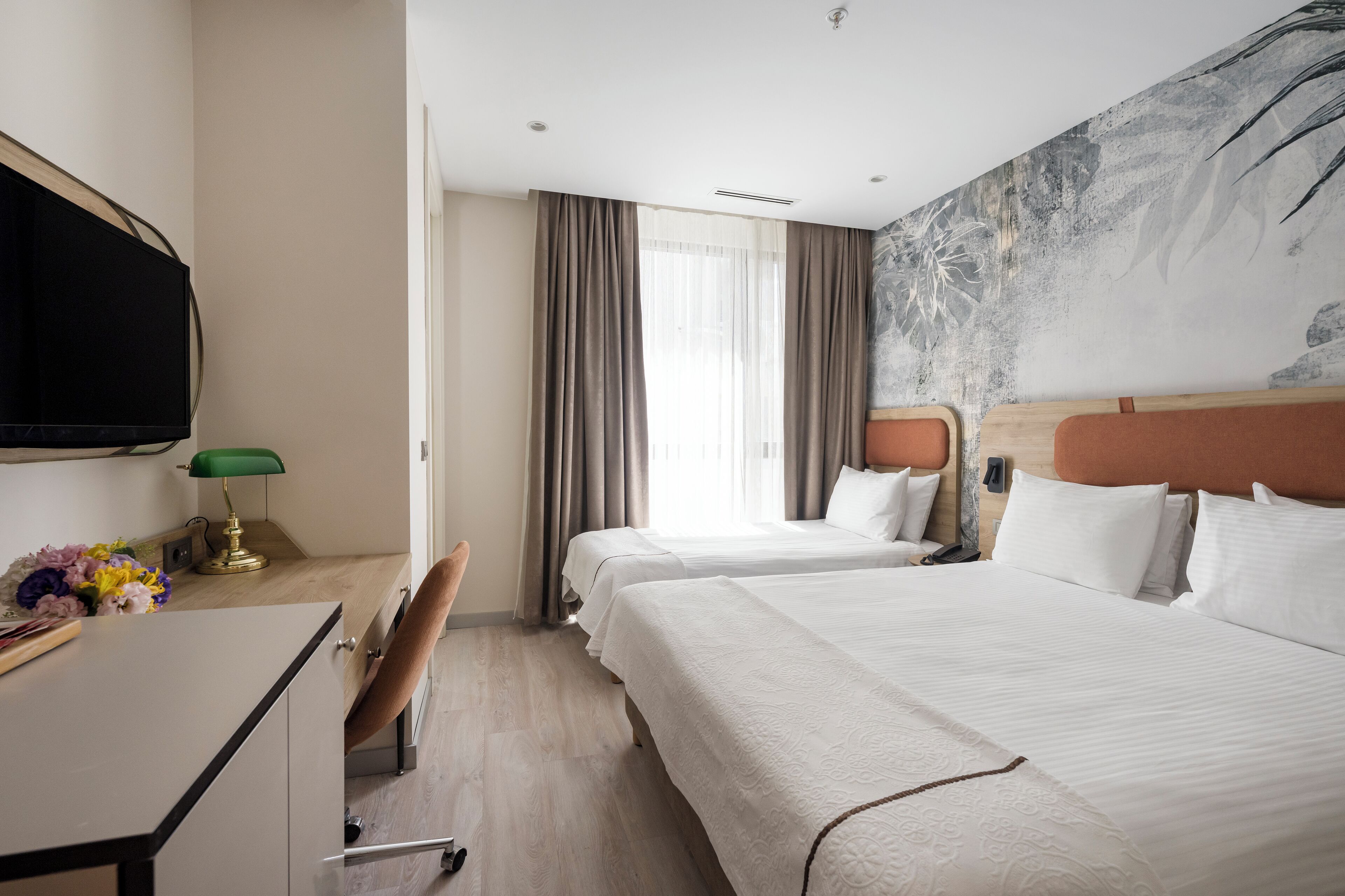 A hotel room with two beds, a desk, a TV, and a large abstract painting on the wall.