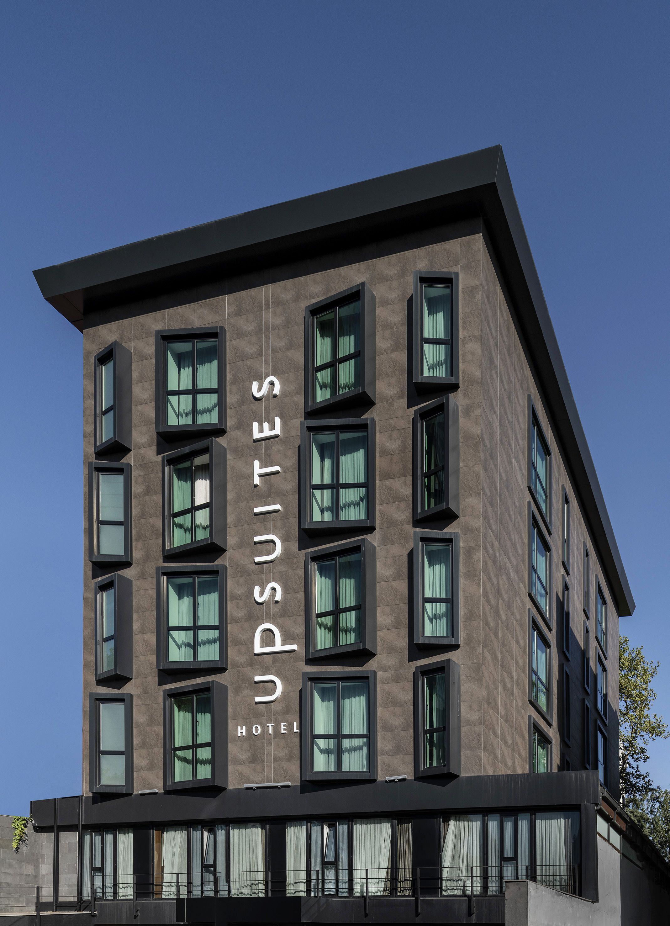A modern hotel building with a name sign 'Upsuites Hotel' on the facade.