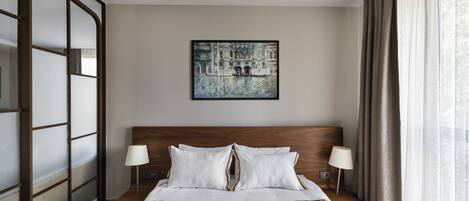 Een hotelkamer met een groot bed, twee bedlampen, een hoofdeinde, een schilderij aan de muur en een raam met gordijnen.