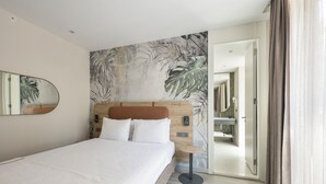 Een moderne hotelkamer met een groot bed, een houten hoofdbord, een grote spiegel en een muurschildering met een tropisch thema.