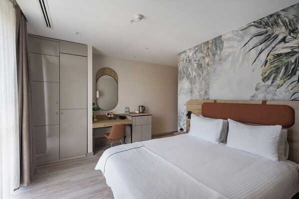 A hotel room with a large bed, a desk with a chair, a wardrobe, and a painting on the wall.