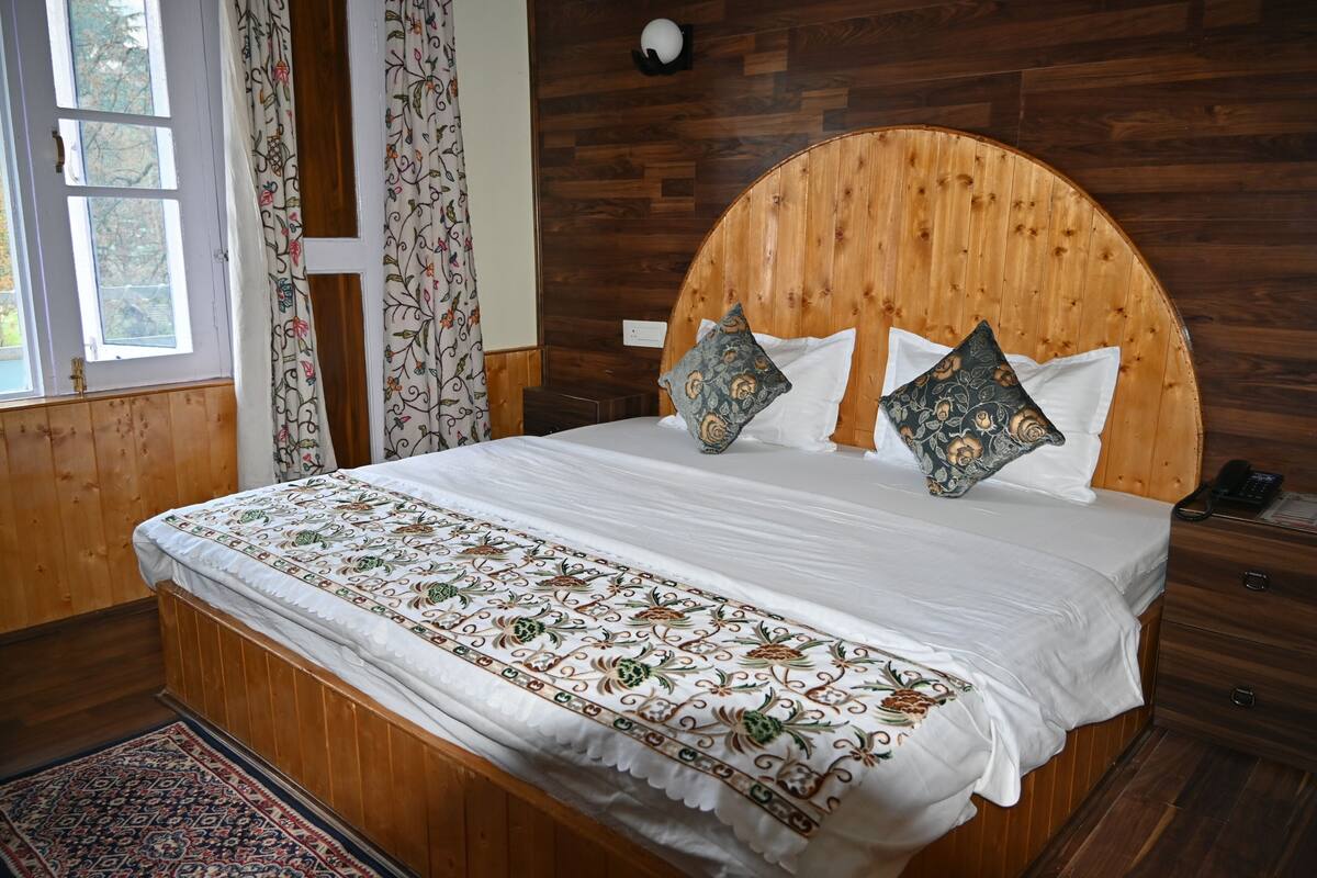 Habitación con paneles de madera, una cama, una mesita de noche y un ventanal con cortinas.