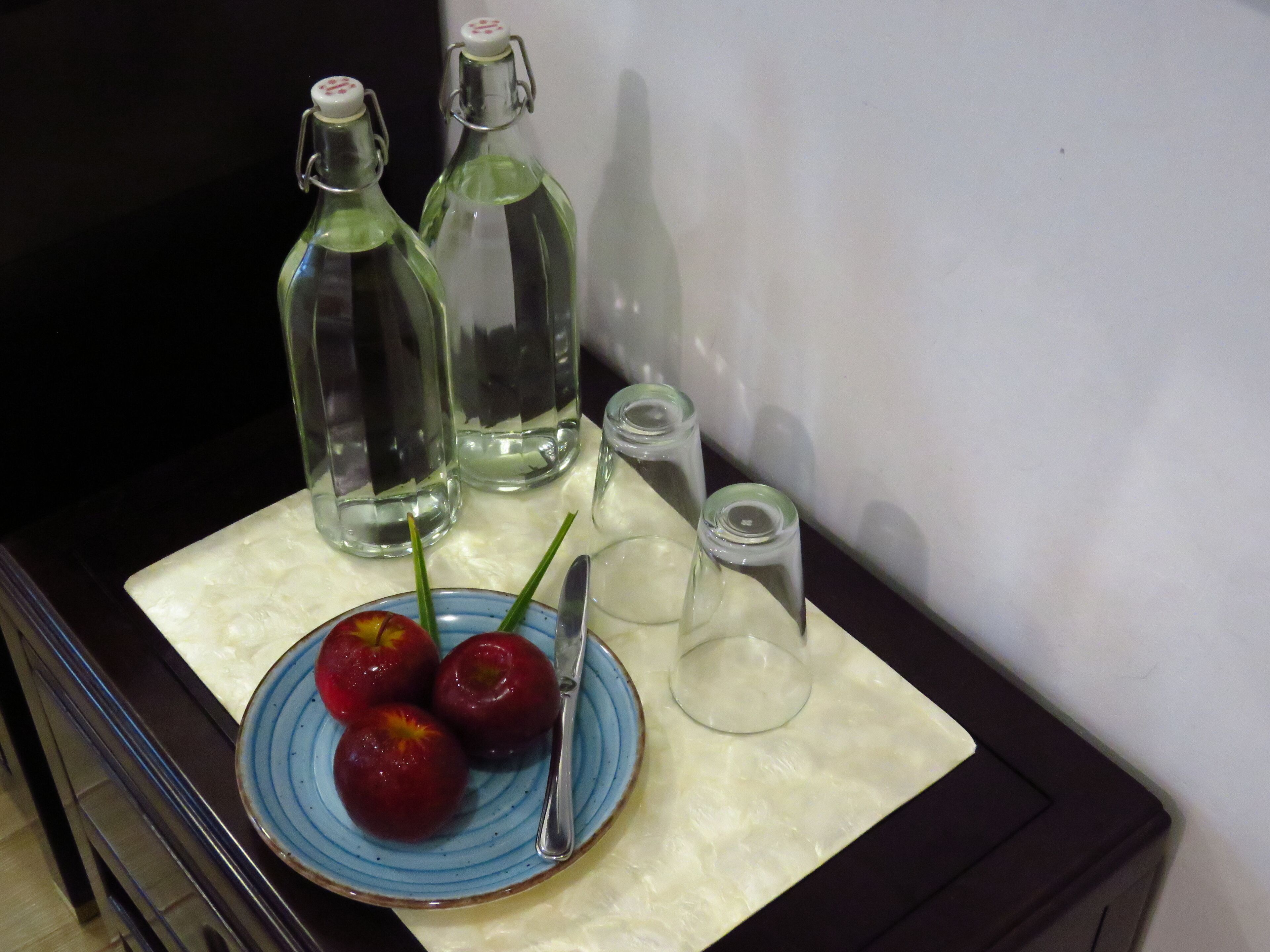 A table with a plate of cherries, a knife, and three glass bottles.