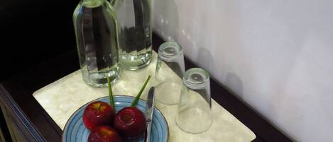 A table with a plate of cherries, a knife, and three glass bottles.