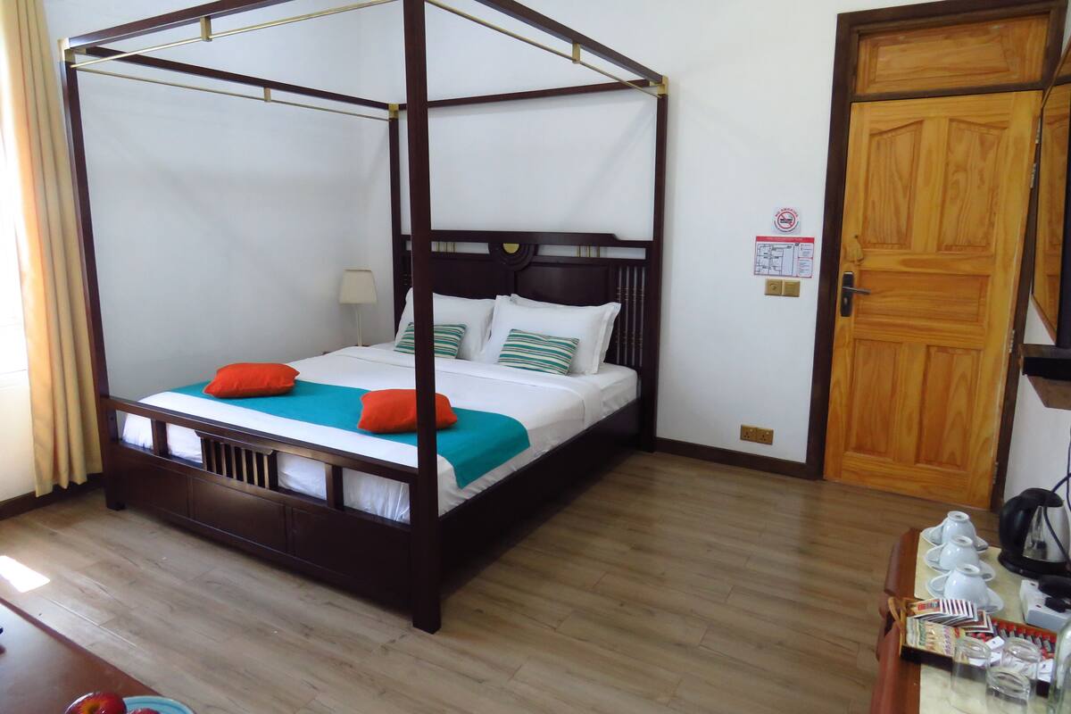 A four-poster bed with a wooden frame, white bedding, and orange pillows.