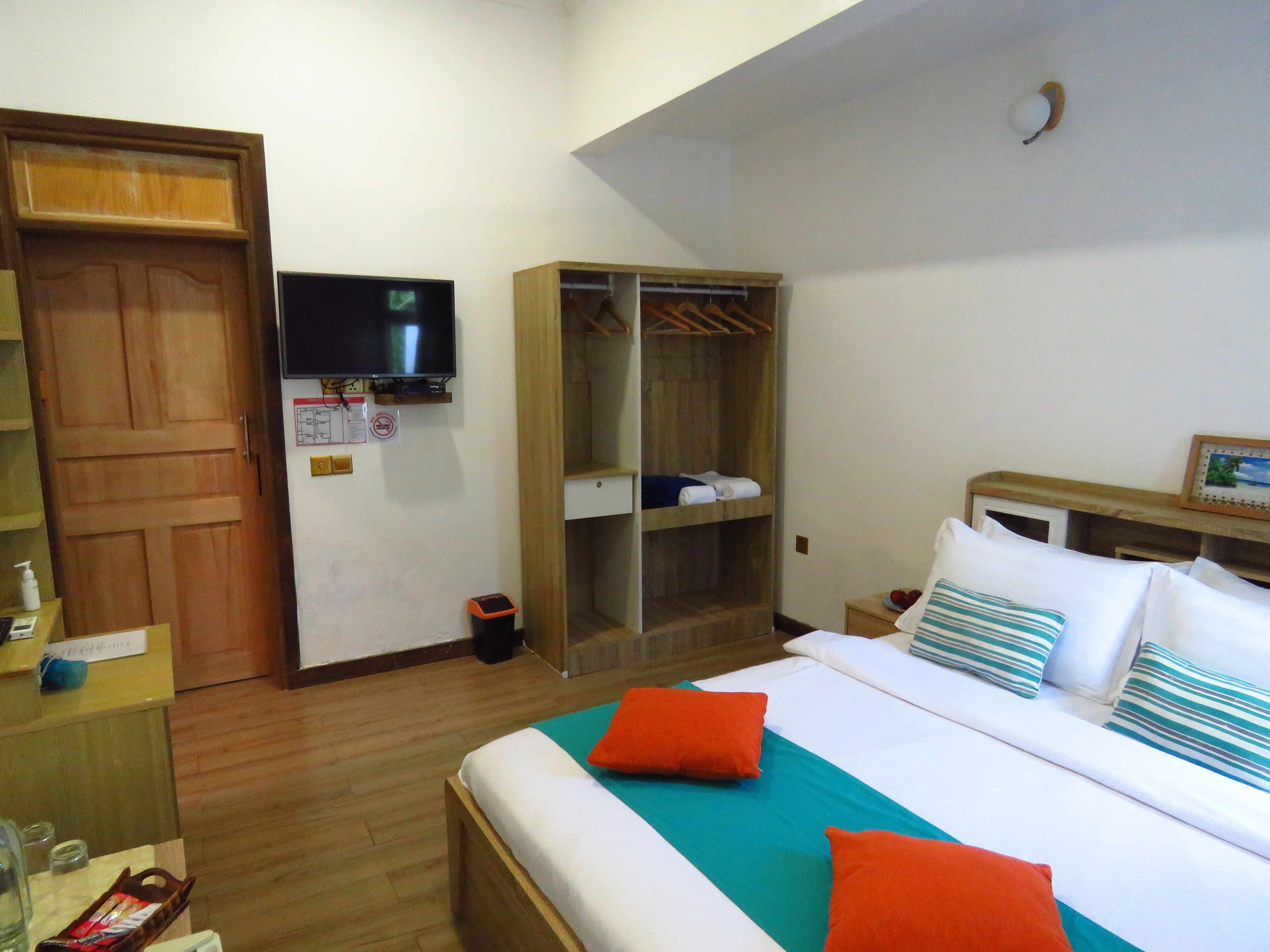 A hotel room with a bed, a TV, a wardrobe, and a small table with a bottle and a glass.