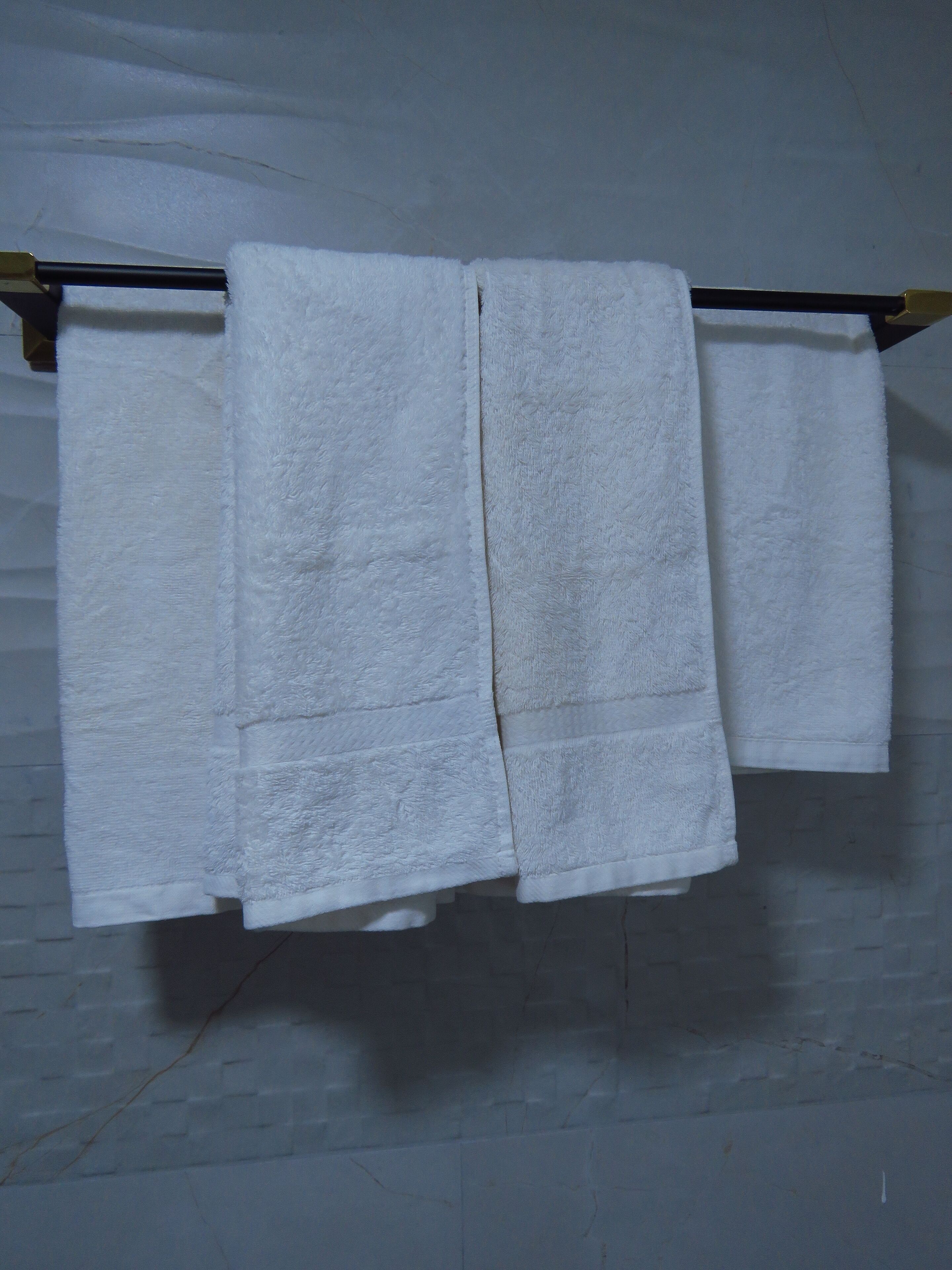 A set of white towels hanging on a metal rack against a white brick wall.