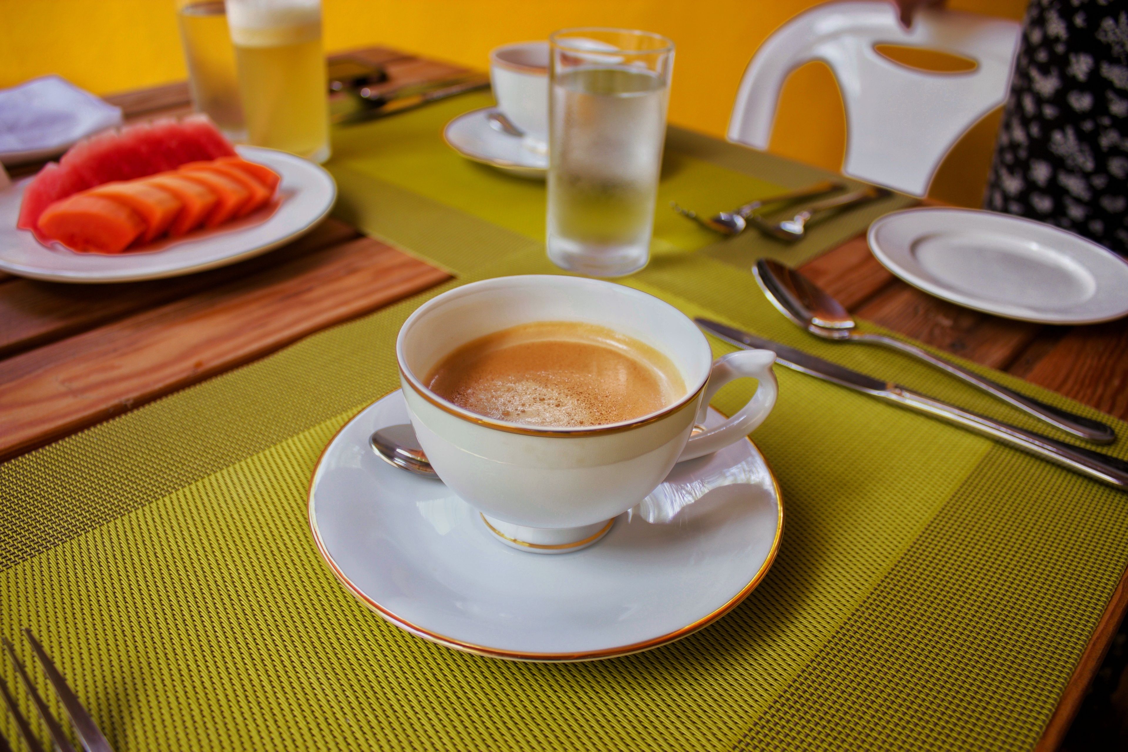 A table with a cup of coffee, a glass of water, and a plate of sliced fruit.