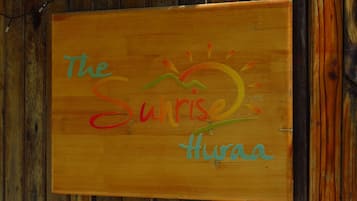 A wooden sign with the text "The Sunrise Huraa" against a wooden wall background.