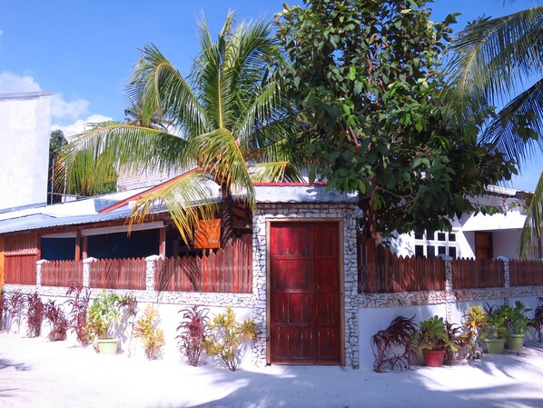 A house with a red door, surrounded by potted plants and palm trees. - The Sunrise Huraa (Huraa)