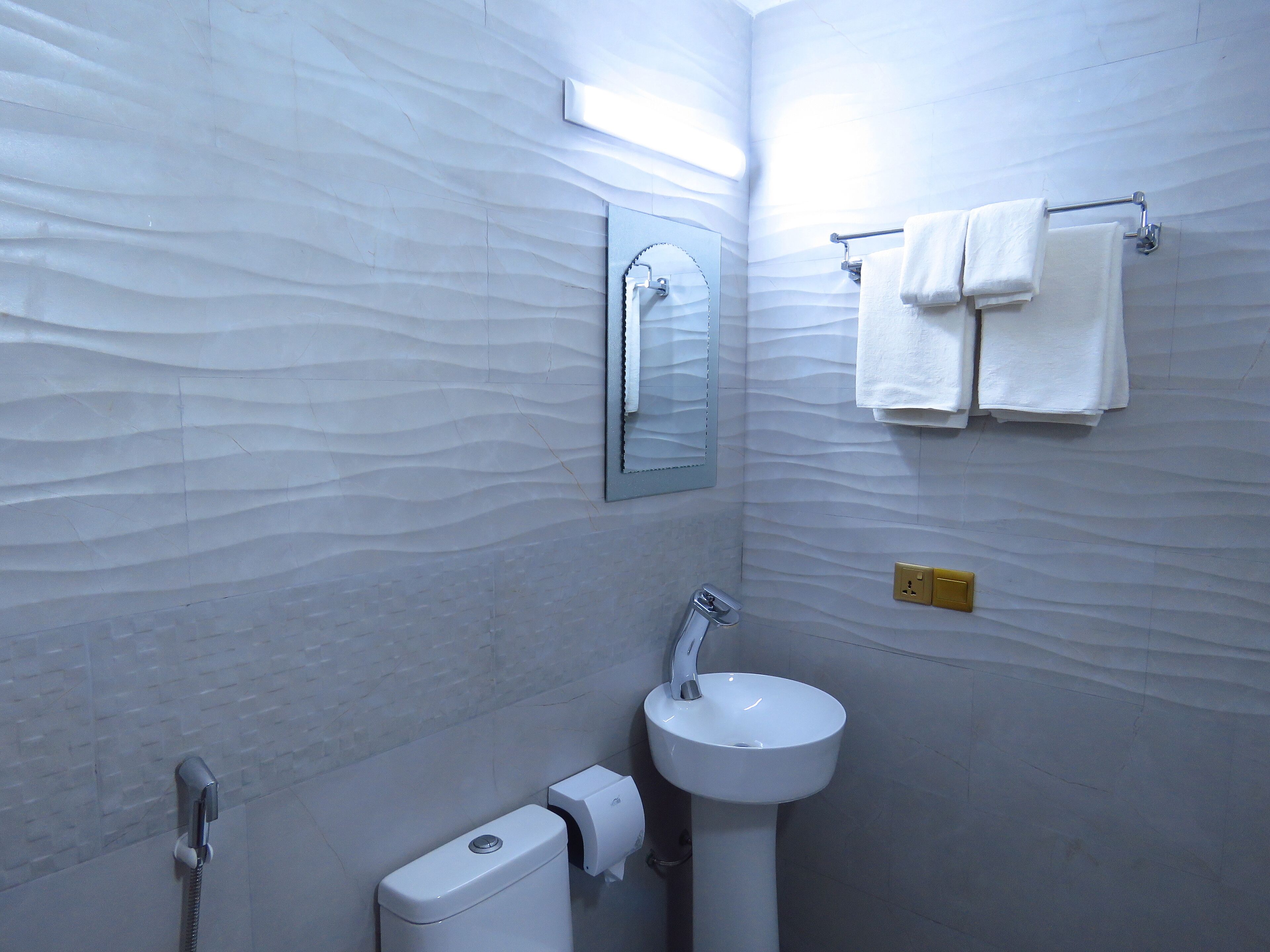 Un baño con pared blanca con textura, un lavabo, un espejo y un perchero con toallas.
