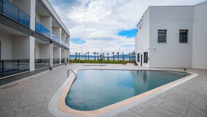A modern pool area with a clear view of the sea, a building with balconies, and a tiled floor. - Sunsan Hotel (Çanakkale)