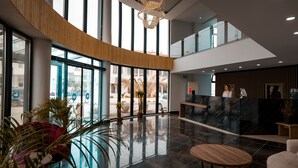 A spacious lobby with a curved wooden wall, a reception desk, and a chandelier. - Sunsan Hotel (Çanakkale)