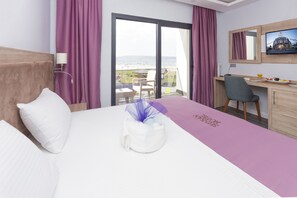 A hotel room with a bed, a desk, a chair, a TV, and a view of the beach. - Sunsan Hotel (Çanakkale)