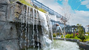 A waterfall feature with the word "SULING" carved into a rock, a small pond, and a metal fence in the background. - Sunsan Hotel (Çanakkale)
