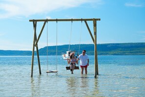 A wooden swing set over a body of water with a boat in the background. - Sunsan Hotel (Çanakkale)