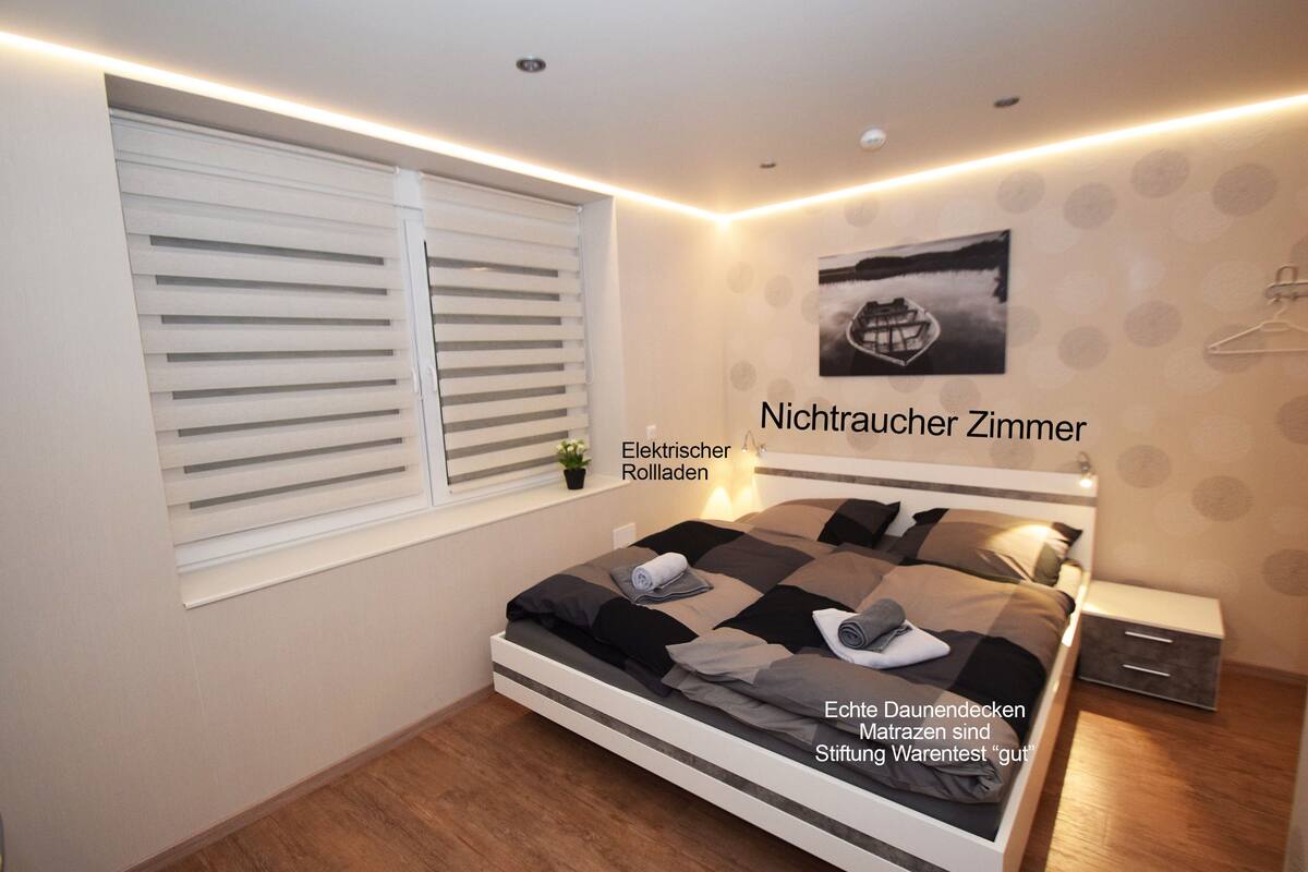 A modern bedroom with a bed, bedside table, and a window with blinds.