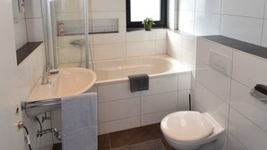 A modern bathroom with a glass-enclosed shower, a bathtub, a toilet, and a sink. - Ferienzimmer 1 Saarlouis (Saarlouis)