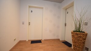 A hallway with two doors labeled 3 and 2, wooden flooring, and a large woven plant pot. - Ferienzimmer 1 Saarlouis (Saarlouis)