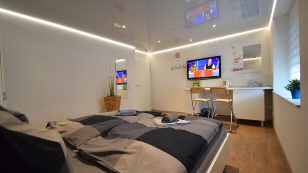 A modern hotel room with a neatly made bed, a desk with a chair, a television, and a small potted plant. - Ferienzimmer 1 Saarlouis (Saarlouis)
