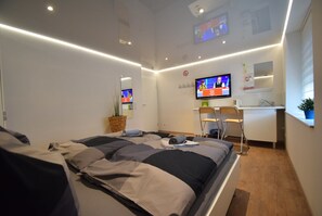 Una habitación de hotel moderna con una cama bien hecha, un escritorio con silla, un televisor y una pequeña planta en maceta.
