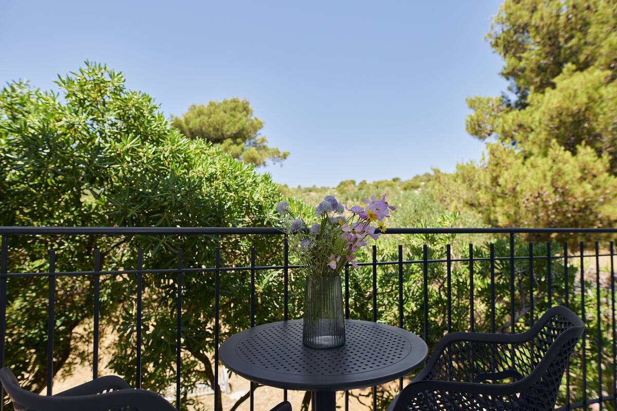 A round metal table with a vase of flowers, surrounded by greenery and a metal fence.