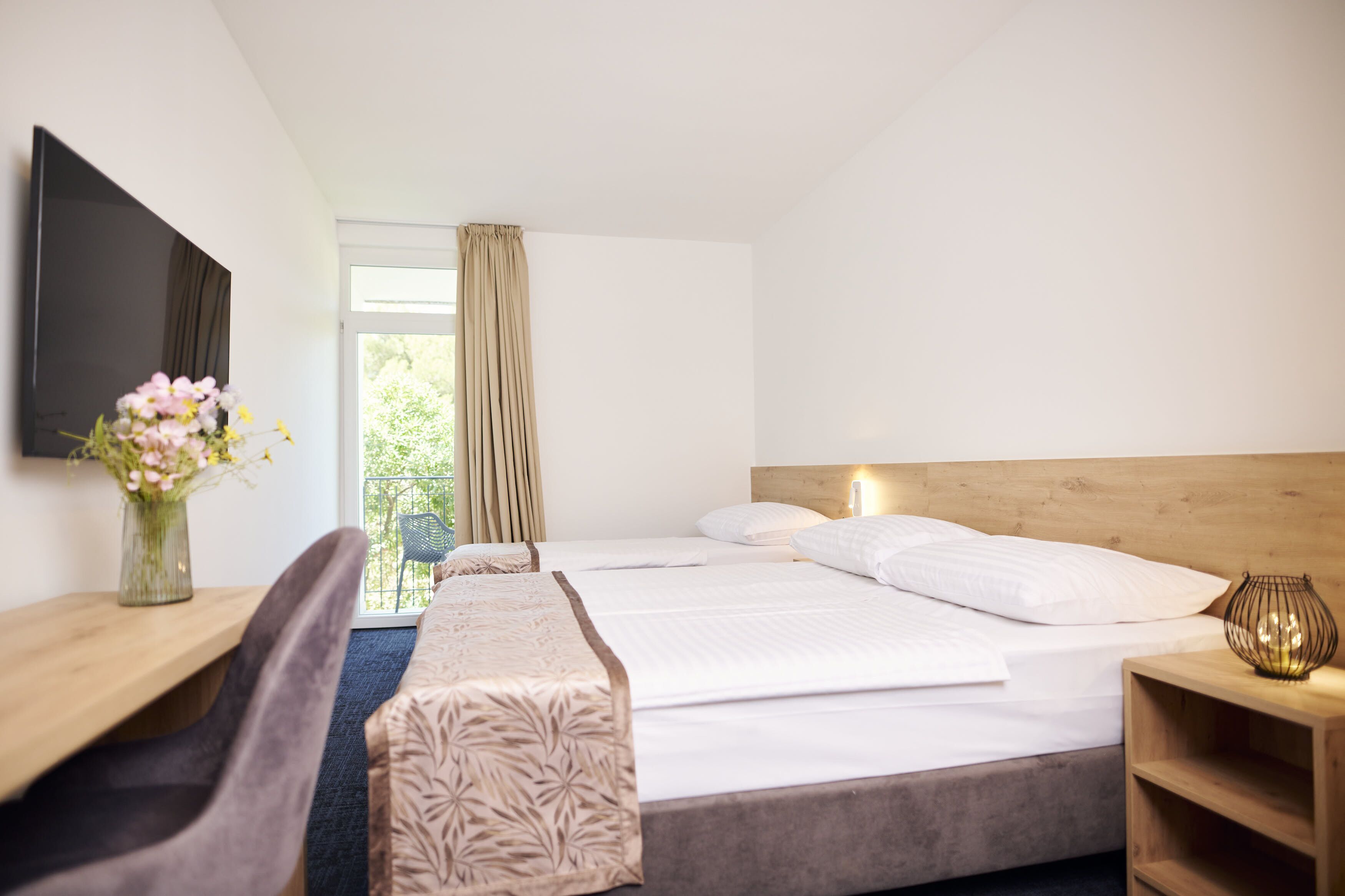 A hotel room with a large bed, a desk, a chair, a TV, and a window with curtains.