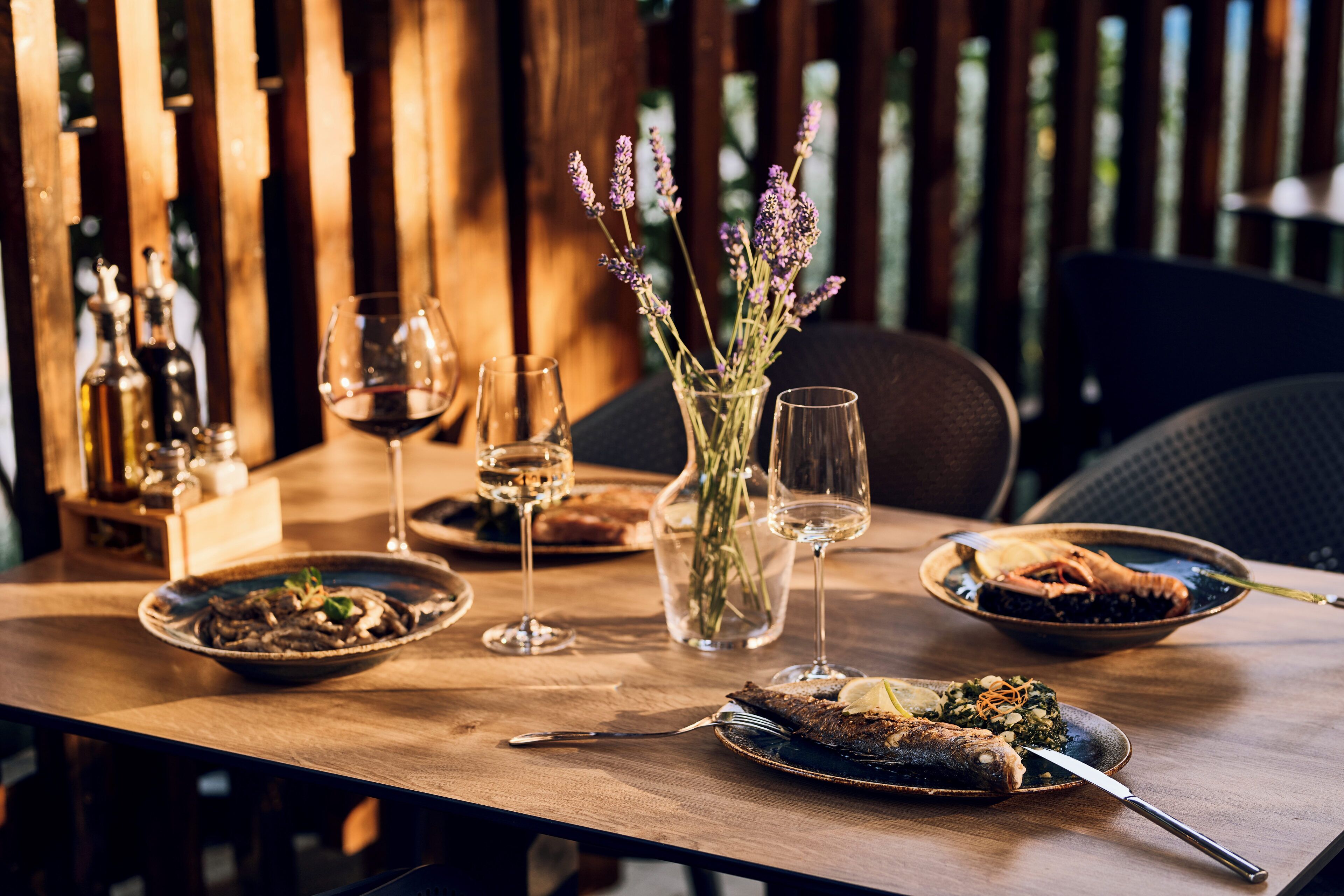 A wooden dining table with plates of food, wine glasses, and a vase with flowers.