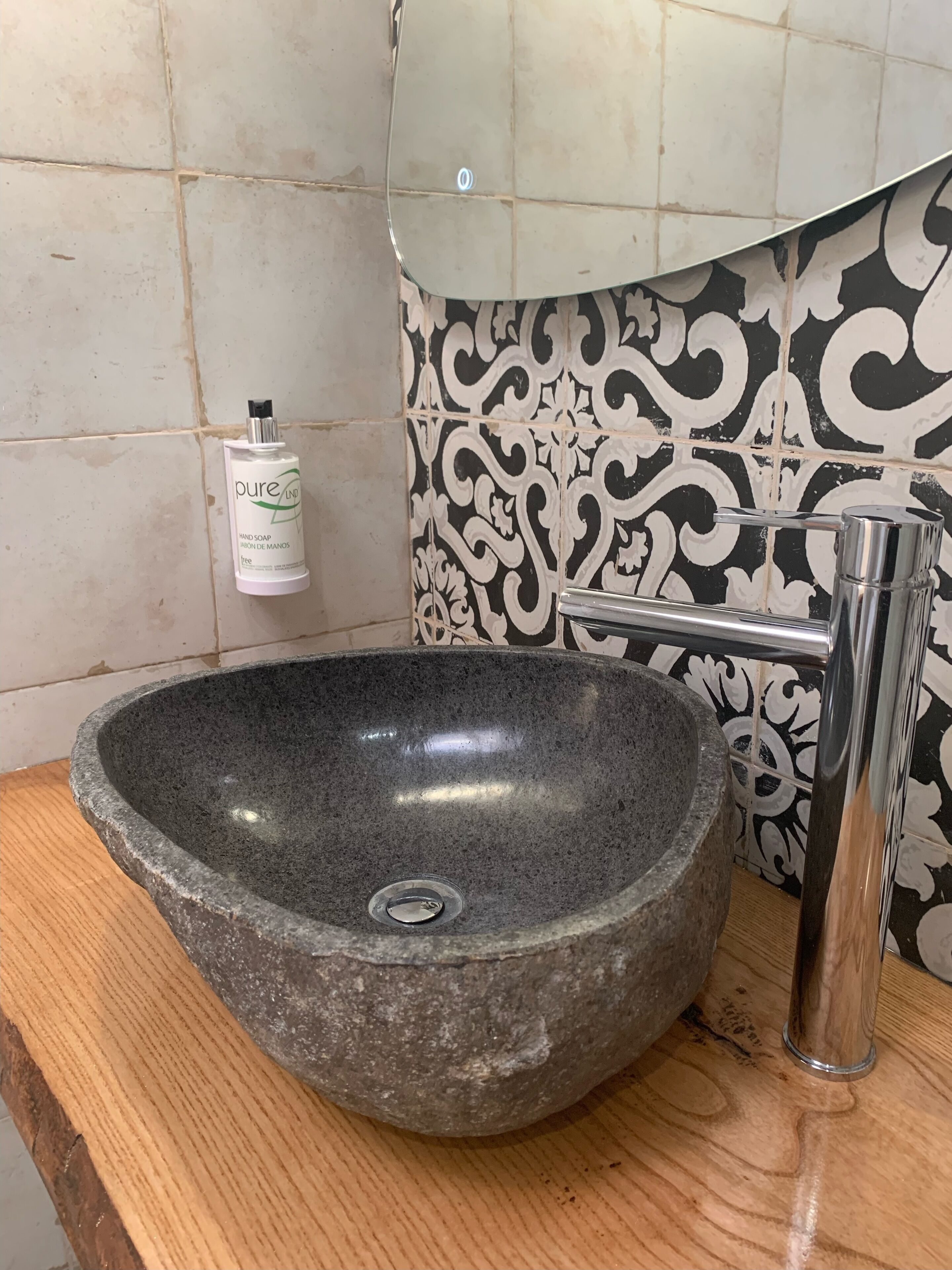 A stone sink with a faucet, a soap dispenser, and a patterned tile backsplash.