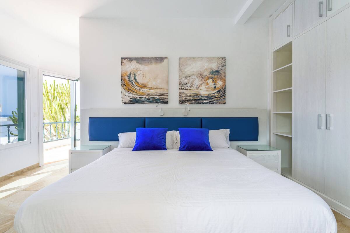A modern bedroom with a large bed, a blue headboard, and two abstract paintings on the wall.