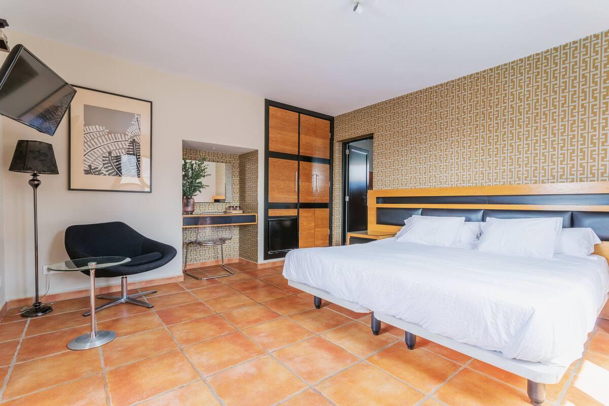 A modern hotel room with a large bed, a desk, a chair, and a TV.