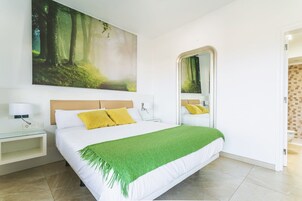 A modern bedroom with a large bed, a green throw blanket, and a forest-themed painting above the bed.