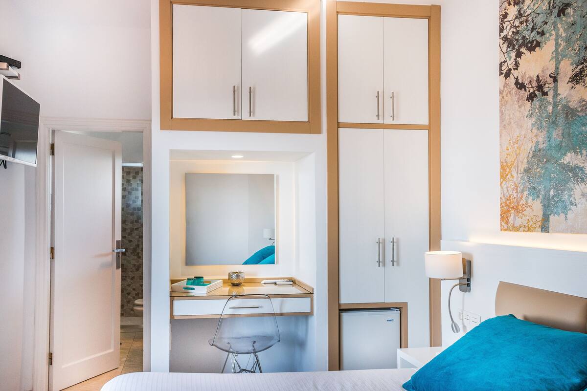 A bedroom with a bed, a desk, a mirror, and a wardrobe.