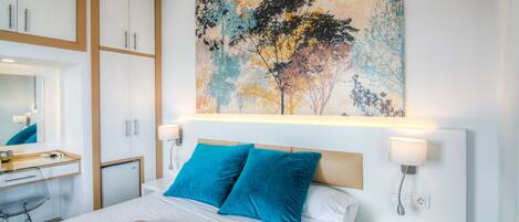 A hotel room with a bed, a desk, a chair, a mirror, and a painting on the wall.