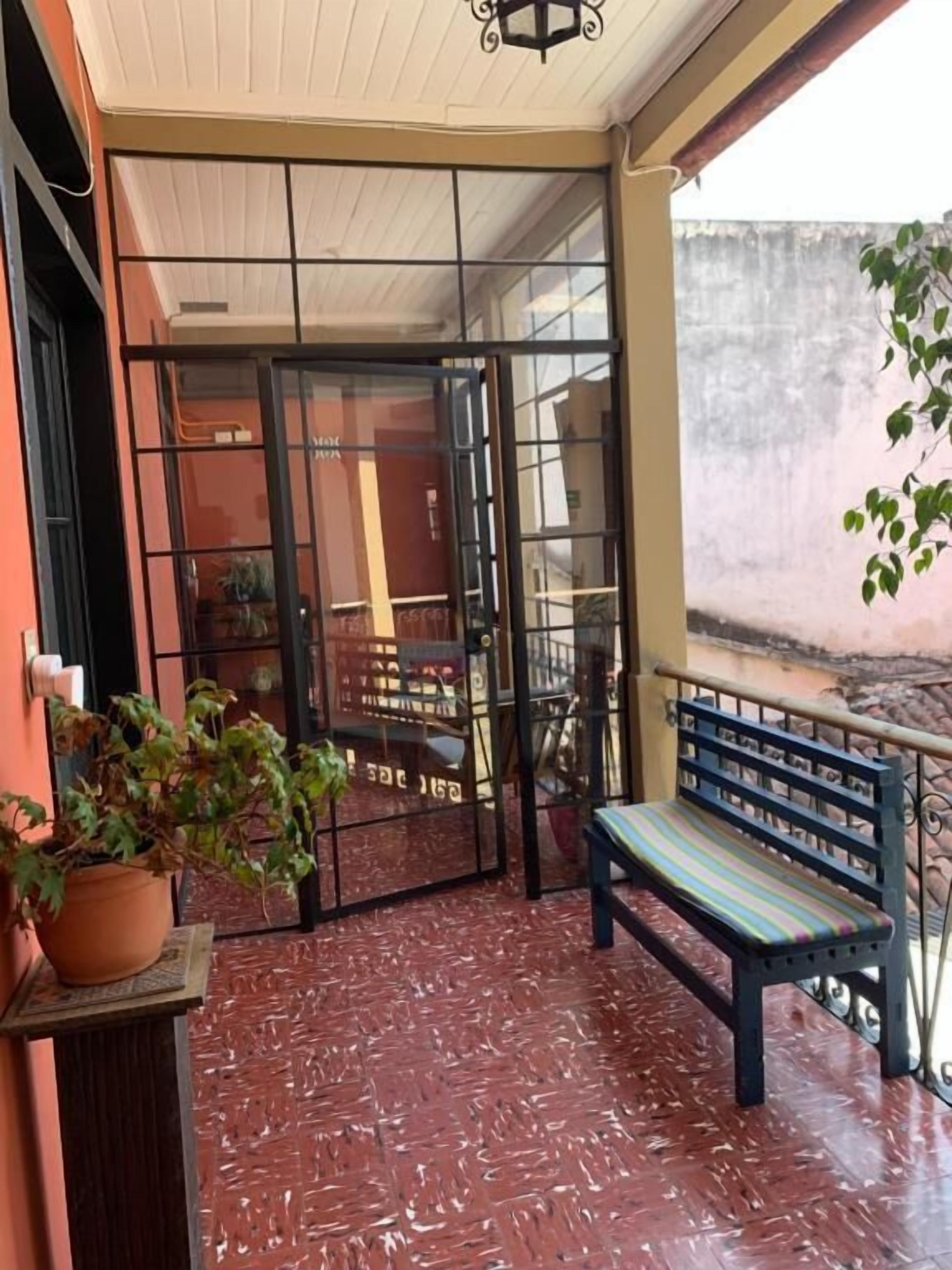 A covered outdoor area with a bench, a potted plant, and a glass door leading to an interior space.