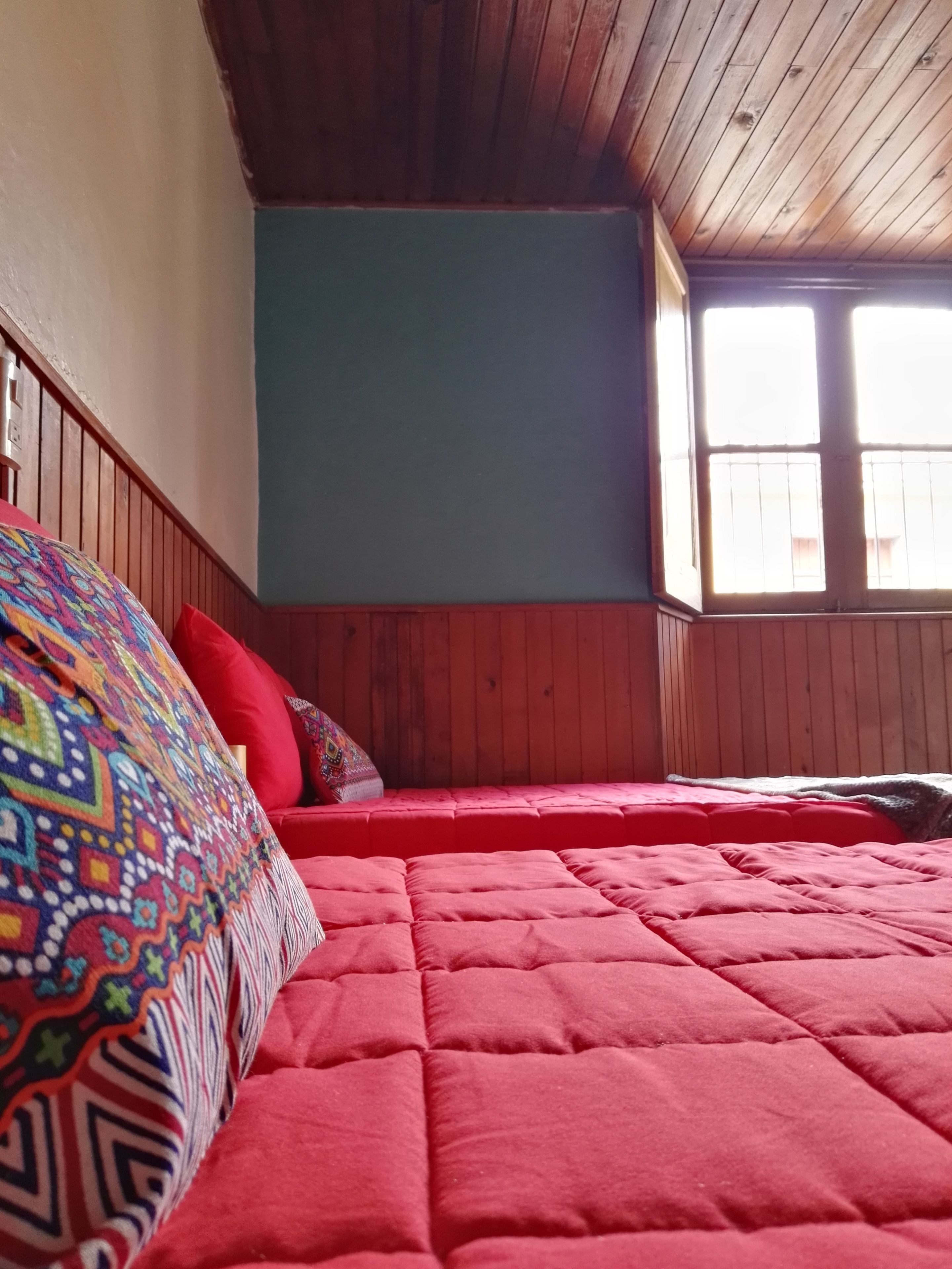 A bedroom with a wooden ceiling, a red bedspread, and a colorful blanket.