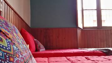 A bedroom with a wooden ceiling, a red bedspread, and a colorful blanket.