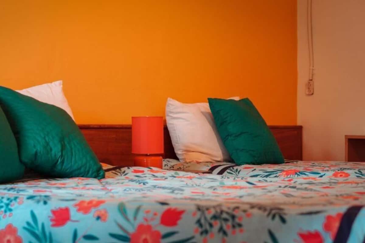 A bed with floral bedding, green and white pillows, and a red bedside lamp.
