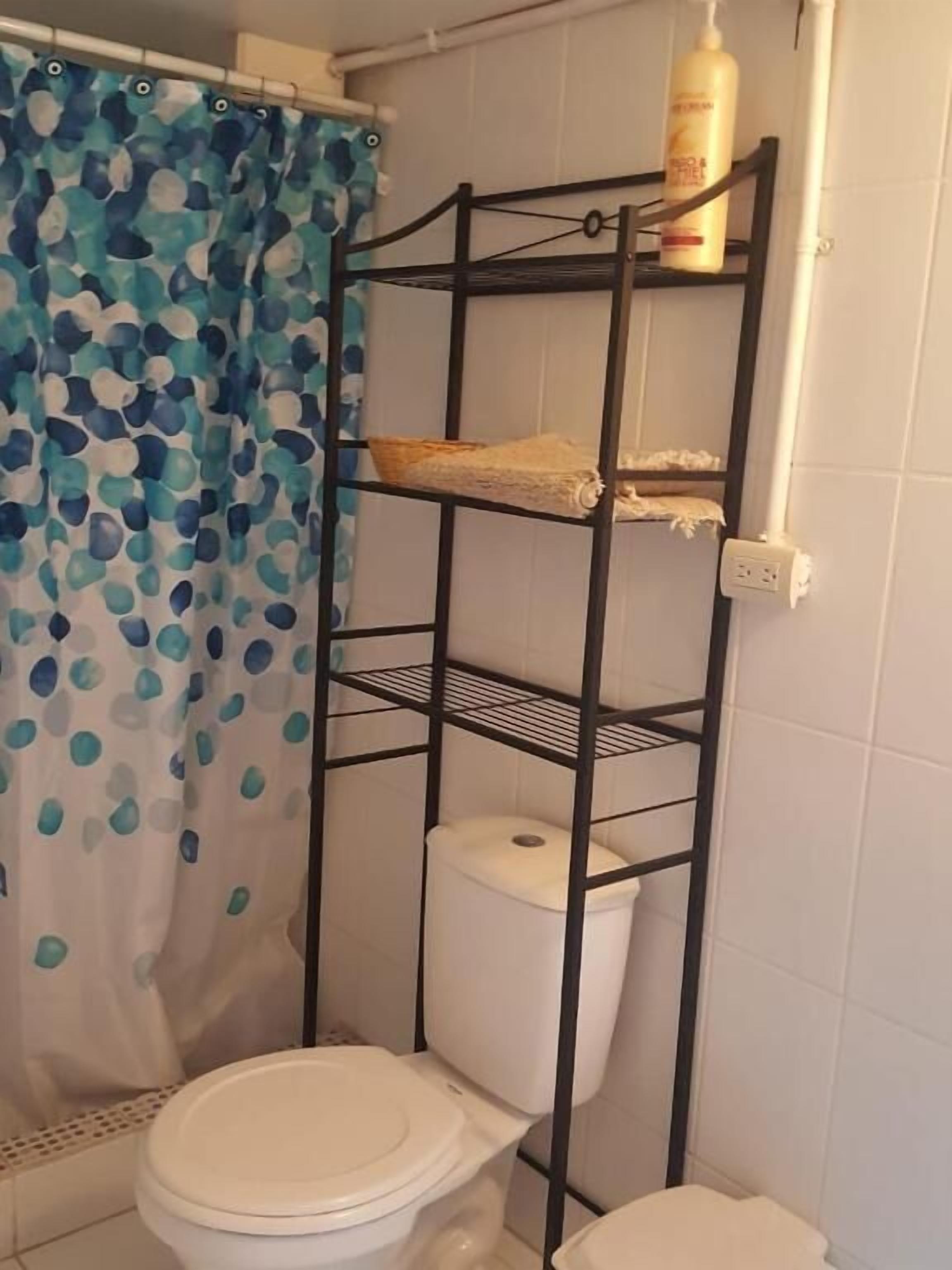 Un baño con inodoro, estante y cortina de ducha.