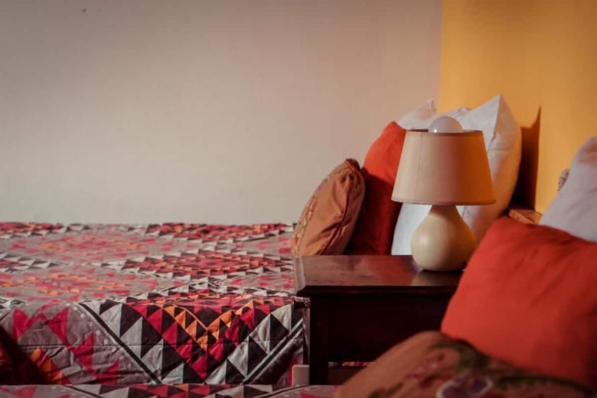 A bed with a patterned quilt, a wooden nightstand with a lamp, and multiple pillows.