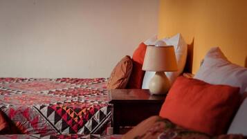 A bed with a patterned quilt, a wooden nightstand with a lamp, and multiple pillows.