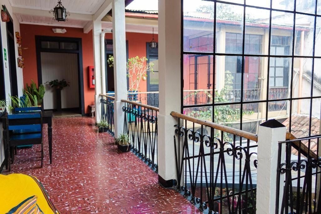 A corridor with a red tiled floor, black metal railings, and potted plants.