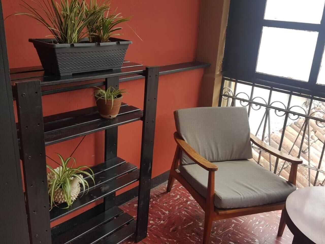 Un balcón con una silla, barandilla de metal y plantas en macetas sobre una repisa.